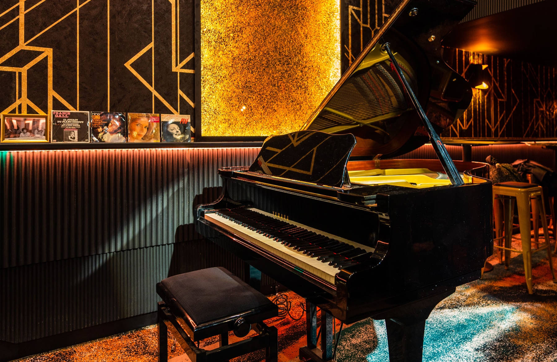 Le salon piano de La Groupie : piano à queue noir devant un mur doré Art déco